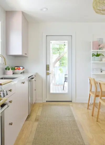 Uitzicht richting keukenverandadeur in geschilderde mauve roze Ikea-keuken met juteloper