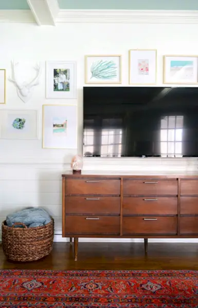 moderne kunstgalerijmuur in witte woonkamer met blauw plafond en vintage tapijt