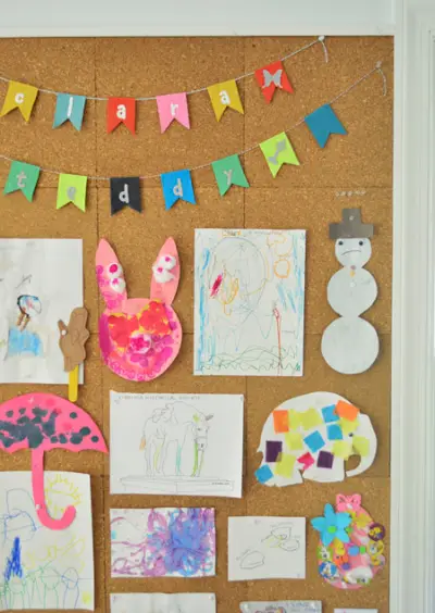 Iš arti vaikų meno detalės, pakabintos ant kamštienos lentos, įskaitant vardinę reklamjuostę iš etsy