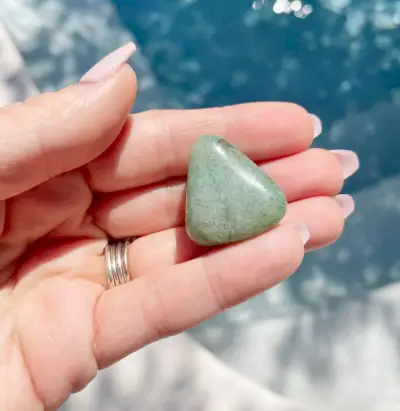 Hand met groene aventurijn gepolijste edelsteen boven water