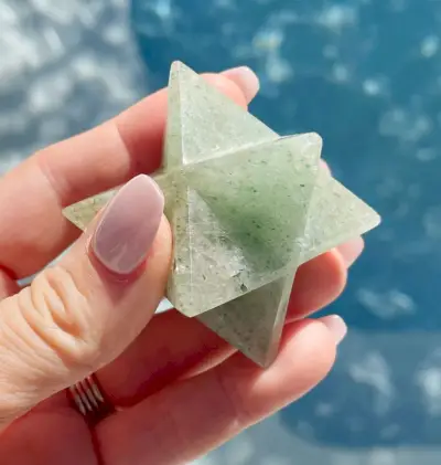 Hand met groene aventurijn merkaba-asteroïde boven water