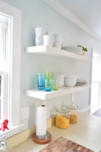 twee lange zwevende Ikea-planken in een keuken met kleurrijke kopjes en stapels wit serviesgoed