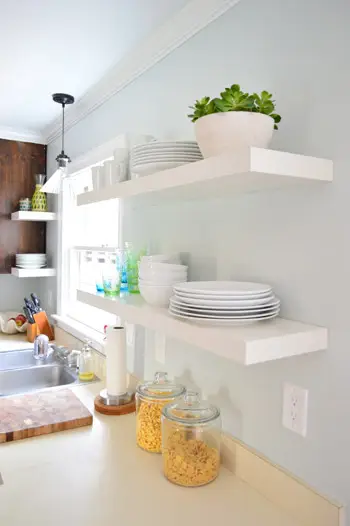 twee paar witte Ikea LACK-planken hingen in de keuken met witte borden, kommen en kleurrijke kopjes