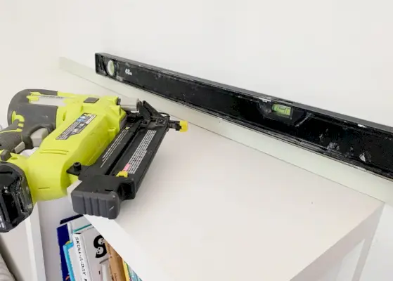 Spijkerpistool naast de eerste strook houtrooster bevestigd aan de muur met niveau