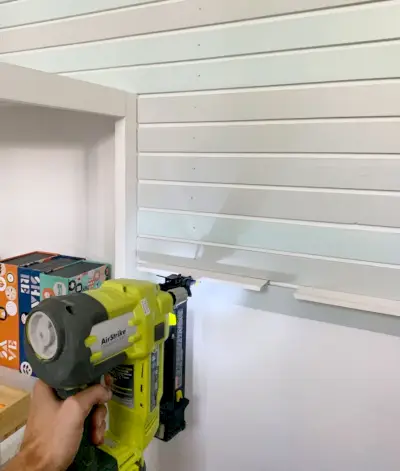 Spijkerpistool dat kleinere roosterstukken aan de muur naast de boekenplank bevestigt