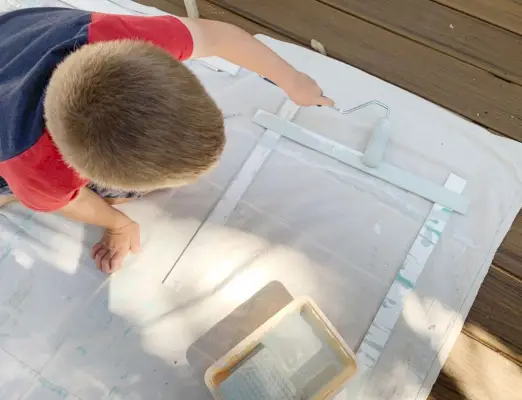 Jonge jongen die een stuk hout schildert met een kleine schuimroller