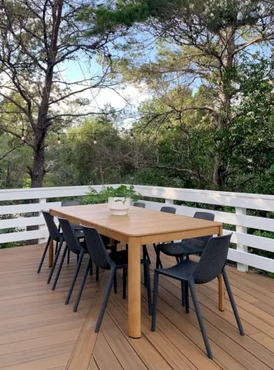 Buiteneettafel van imitatiehout en metaal met zwarte stoelen omgeven door bomen