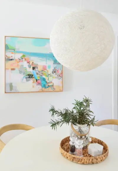 Grote String Globe hanglamp boven witte tafel met strandachtige kunst op de achtergrond