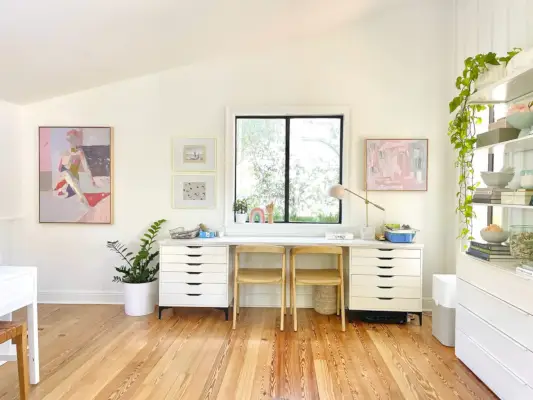 Kinderkunstbureau onder raam in open moderne witte familiekamer met beschadigde plafonds en kunstwerken