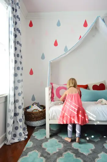 Meisje speelt op bed onder de laatste regendruppelmuurschildering over een stoffen hemelbed
