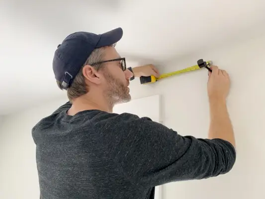 John meet de muur boven het raam terwijl hij de gordijnroedehaak vasthoudt