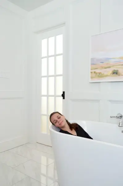 Sherry zittend in vrijstaand bad in moderne traditionele badkamer met marmeren vloer en wandafwerking