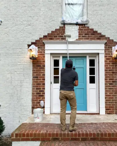 schilder die de veranda van een bakstenen huis wit schildert