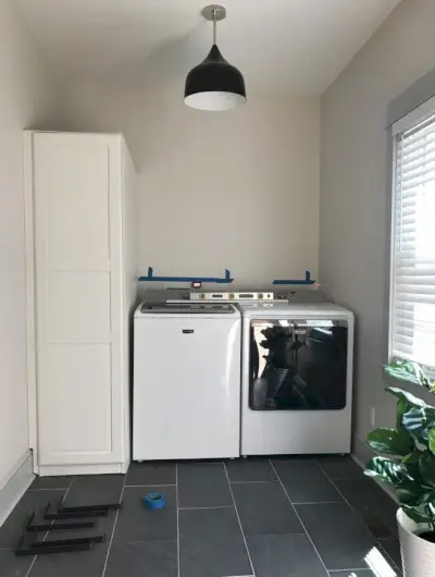 Ikea pax kledingkast geplaatst naast bovenlader wasmachine en droger in wasruimte