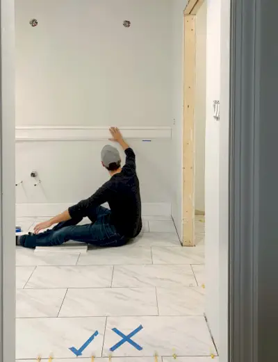 John houdt een proefstuk van de wandlijst in de badkamer vast