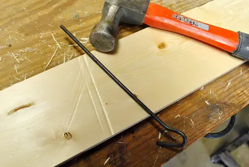 gebruik een metalen staaf en een hamer om lange deuken in een nieuw houten bord te maken, zodat het er oud en versleten uitziet