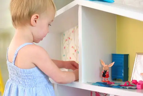 Close-up van een klein meisje dat speelt met Olivia Pig-beeldjes in een zelfgemaakt poppenhuis