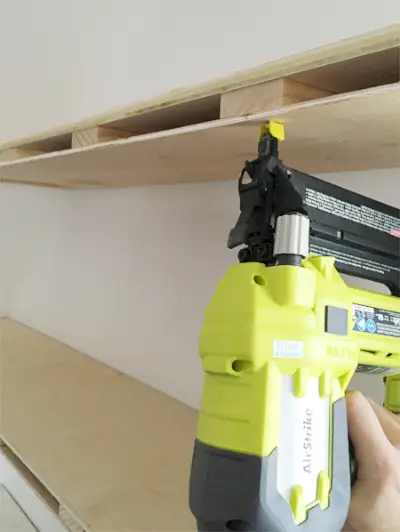 Een Ryobi-krachtspijkermachine om dunne multiplexplaten aan de onderkant van doe-het-zelf zwevende planken te bevestigen