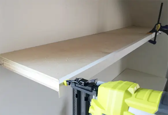Een Ryobi-krachtspijkermachine die gezichtsstukken van 1x2 grenenhouten planken bevestigt aan dunne witte zwevende planken in de bonuskamer