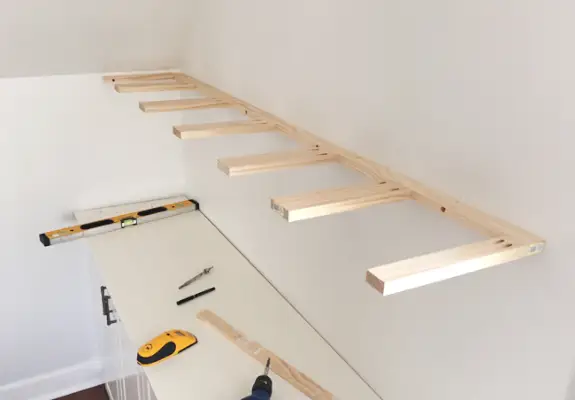 Een stuk zelfgemaakt dun houten zwevende plankje dat aan de muur wordt gehangen met behulp van 1x3 en 1x2 grenen planken