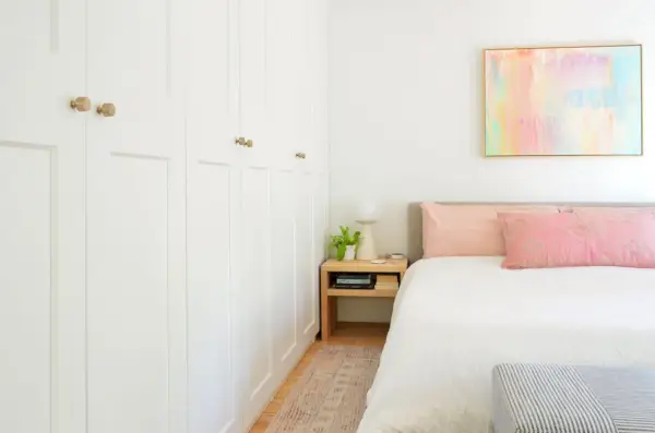 Muur van Ikea Pax-kasten naast kingsize bed met kleurrijk schilderij