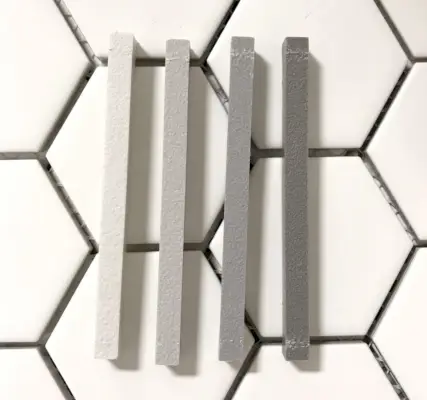vier monstersticks van mapei-specie bovenop een witte zeskantige tegel, gaande van licht naar donker