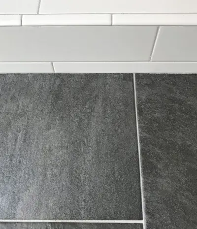 witte metrotegeldouche naast donkere leistenen vloer met dezelfde grijze voeg