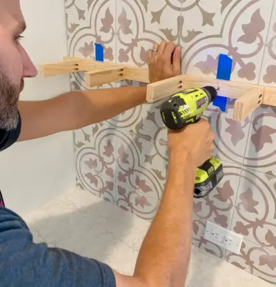 Man boort door tegelwand met houten steunbeugel omhoog