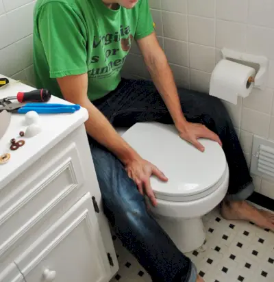 John zit op de achterkant van de toiletpot om hem op zijn plaats te drukken