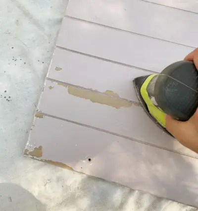 Het schuren van oude verfdruppels van houten kasten ter voorbereiding op het schilderen van de kast