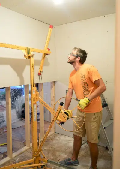 John tilt het gipsplaatpaneel op zijn plaats op de muur van de wasruimte