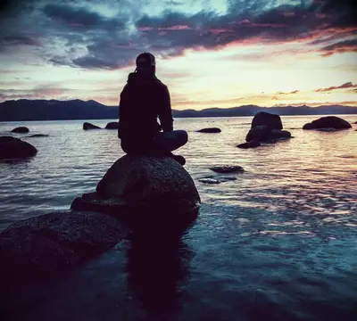 A man staring at the rising sun alone in a bay