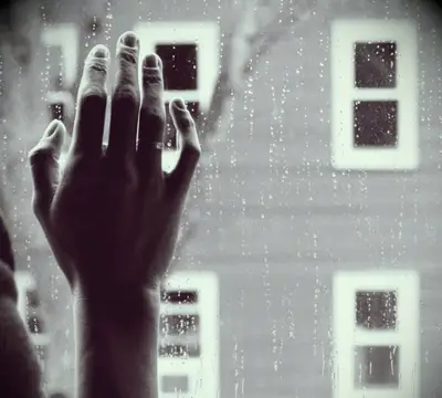 A hand resting against a rainy window