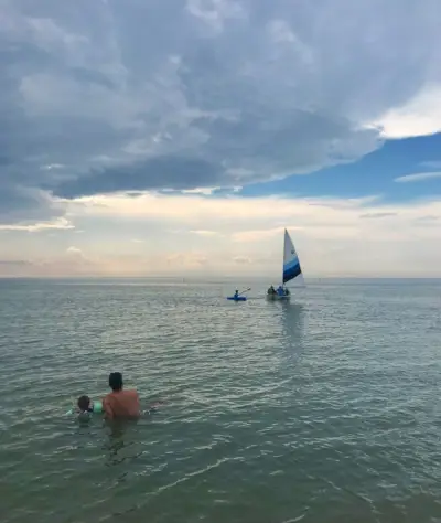 mensen die in het water zitten en naar een zeilboot kijken op het strand van Cape Charles