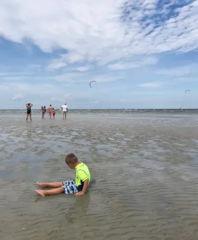kind zit in ondiep en met kiteboarders op het strand van Cape Charles