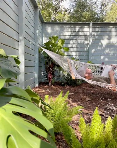 John ligt in een hangmat in de zijtuin tussen tropische aanplantingen