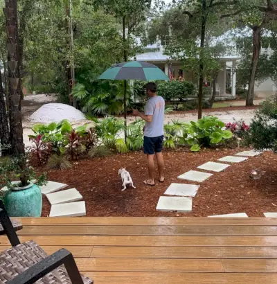 Hamburgerhond die in de voortuin plast, terwijl John een paraplu vasthoudt