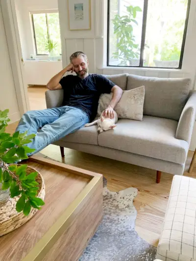 John yanında chihuahua ile gri iki kişilik koltukta oturuyor