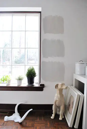 drie grijze verfopties van Benjamin Moore, geschilderd als testvierkanten op een witte muur met houten randen