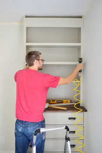 Man spijkert sierstukken op de voorkant van een doe-het-zelf-boekenplank