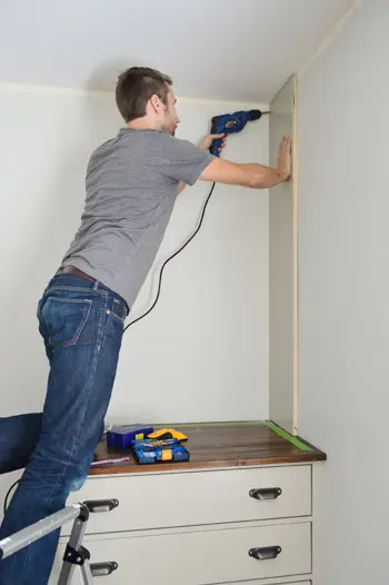 Man die een zijstuk van een boekenplank aan een muur bevestigt