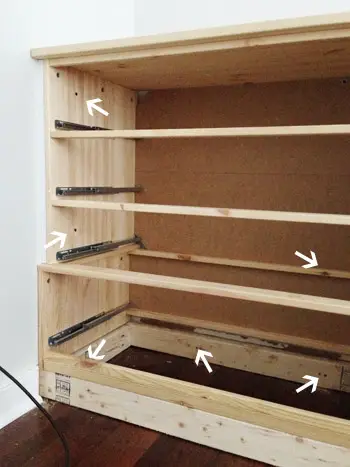 Pijlen wijzen naar schroeven waar de Ikea Fjell-dressoir aan de muur en de 2x4-basis was bevestigd