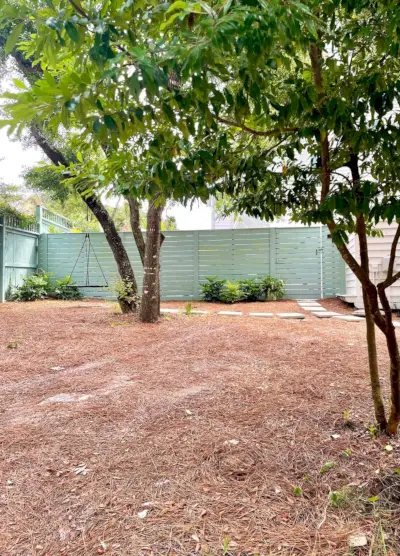 Grote tuin met dennenstro met groen hek op de achtergrond met bandschommel op eik