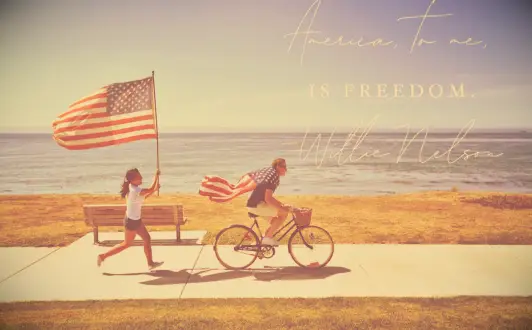 A kie rider draped in a US flag and a woman running with another flag by the sea