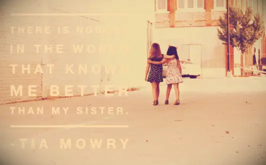 Twin sisters standing arm in arm in downtown Los Angeles by a white brick wall