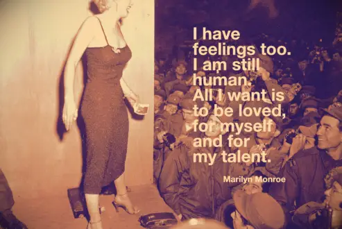Marilyn Monroe onstage at an army base with a cheering crowd of soldiers
