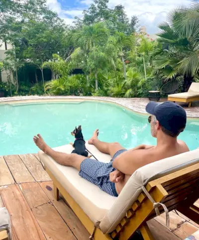 John zit bij het zwembad in Akumal met Penny de hond
