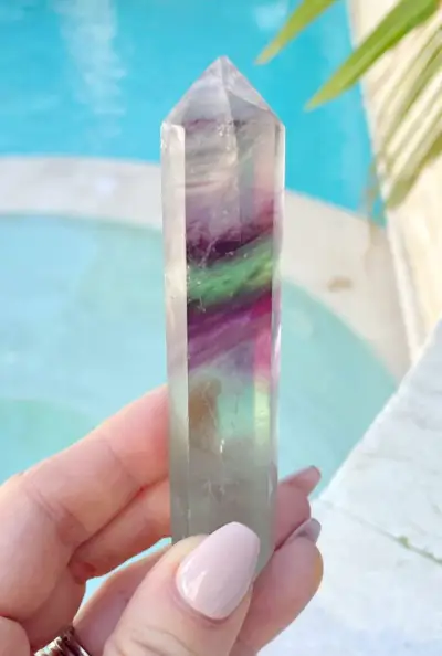 Regenboogfluorietkristalpunt in de hand bij het zwembad