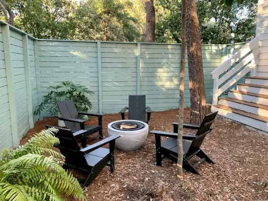 Geschilderde omheinde zijtuin met zwarte Adirondack-stoelen rond vuurplaats met potplanten