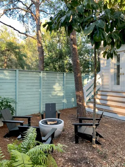 Bomen rond de omheinde zijtuin met zwarte Adirondack-stoelen rond de vuurplaats